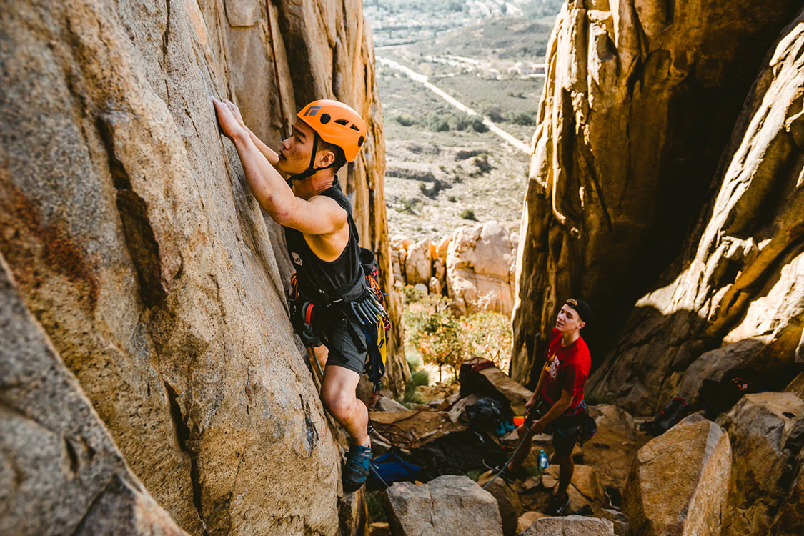 An Asian man rock climbing with a belayer in Mission Trails Regional Park.
