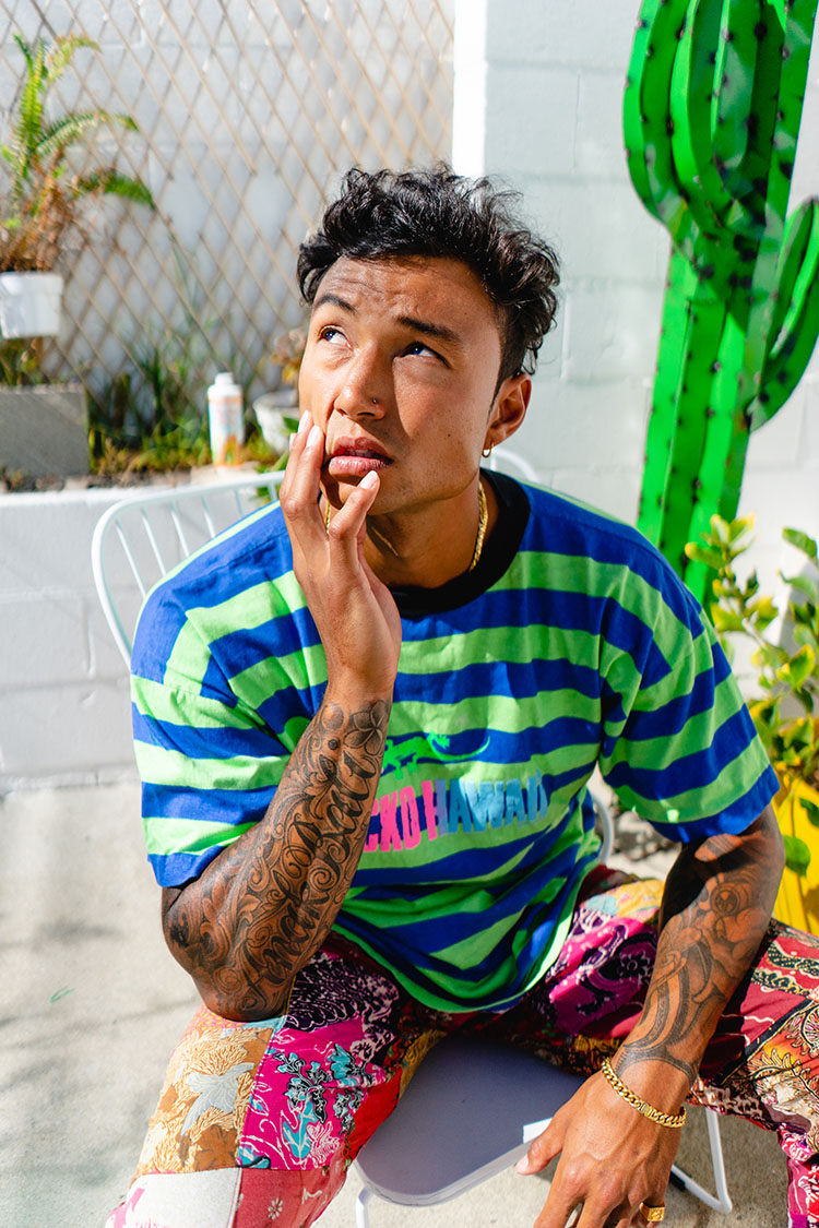 Man in colorful clothes sits on a white chair outside and stares into the sun.