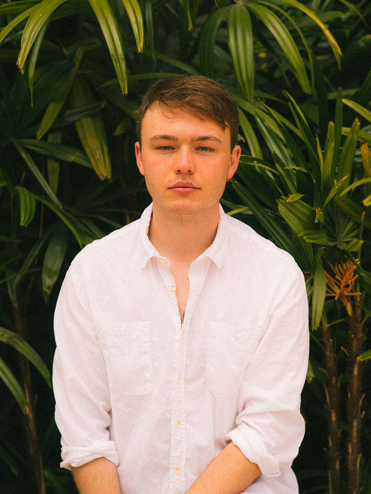 Man in white button-down shirt in front of tropical plants.