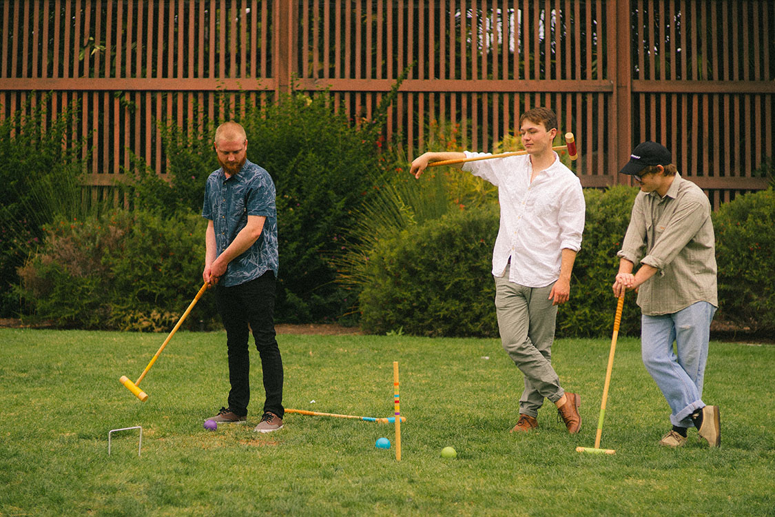 Three men play croquet in front of the Balboa Park Botanical Garden.