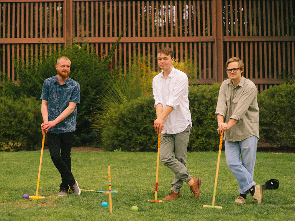 Three men play croquet in front of the Balboa Park Botanical Garden.