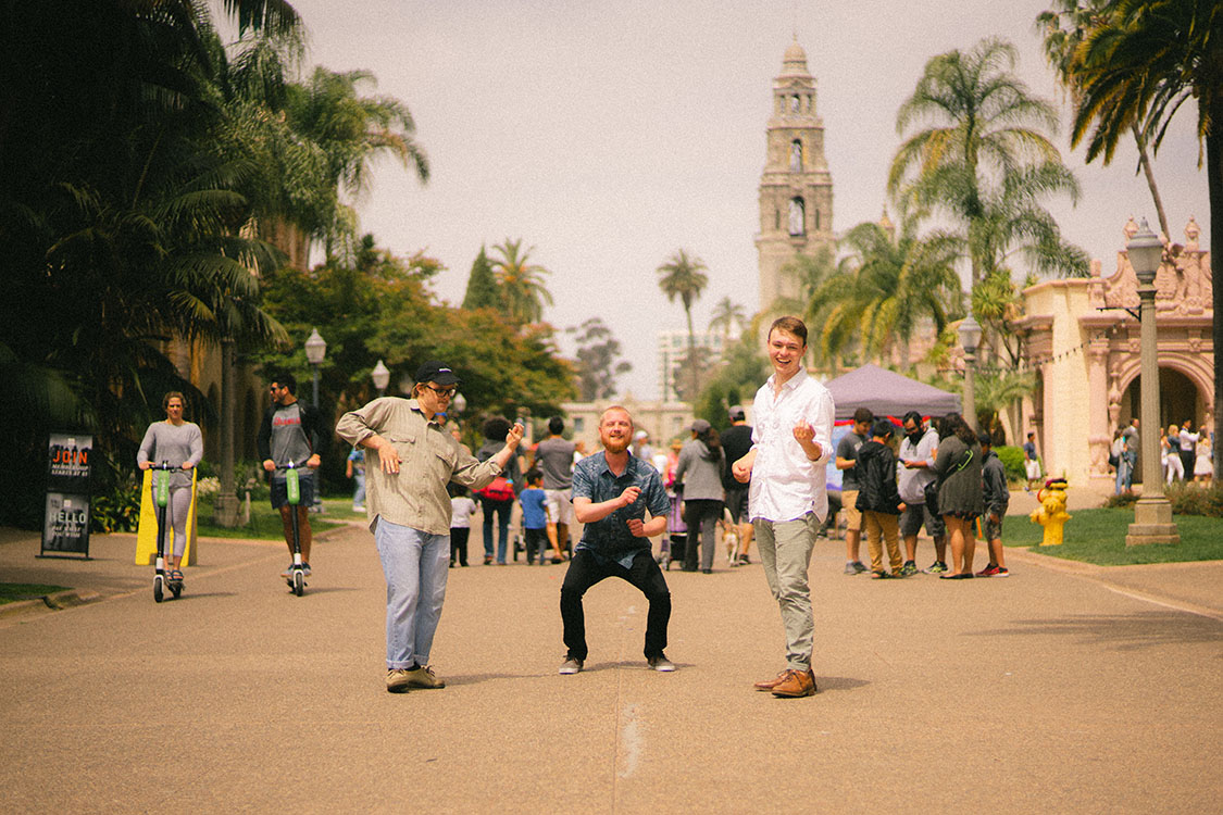Three men play air instruments in Balboa Park.