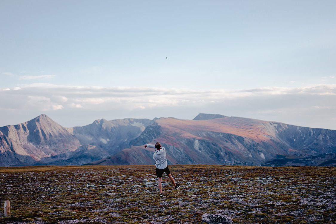 A man alone in Rocky Mountain National Park throwing a rock straight up into the air.